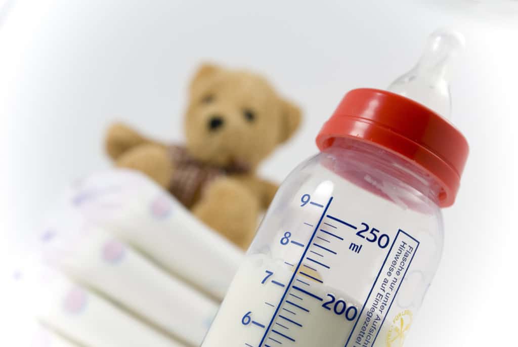 Ein Stapel Windeln, Babyflasche und ein Teddybär vor weißem Hintergrund